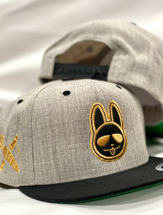 A snapback cap with a heather gray crown and black visor featuring a gold-colored bunny logo on the front.